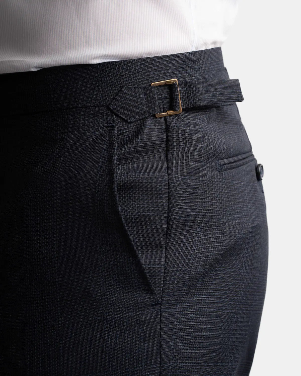 Close-up of a person wearing Cavour's Navy Check Hightwist Wool Suit pants, featuring a side adjuster buckle and subtle check pattern, paired with a tucked-in white dress shirt—ideal for business travel. Includes side and back pockets for convenience. , available at Richard Gelding Mayfair