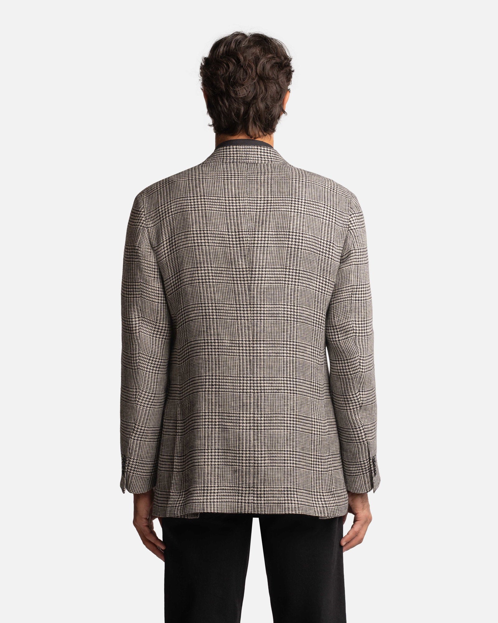 A person with short brown hair is seen from behind, wearing the Cavour Black/Grey Linen Glencheck Blazer paired with black pants, set against a plain white background. , available at Richard Gelding Mayfair