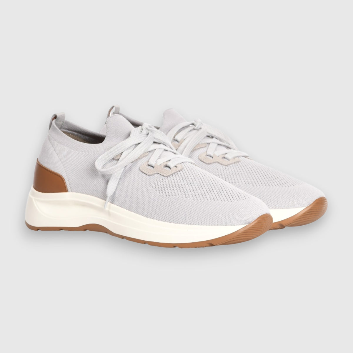 Gran Sasso Light Grey Knitted Sneakers feature white laces, white midsoles, light brown outsoles, and brown heel accents. These comfy, modern low-cut shoes are set against a plain light gray background. , available at Richard Gelding Mayfair