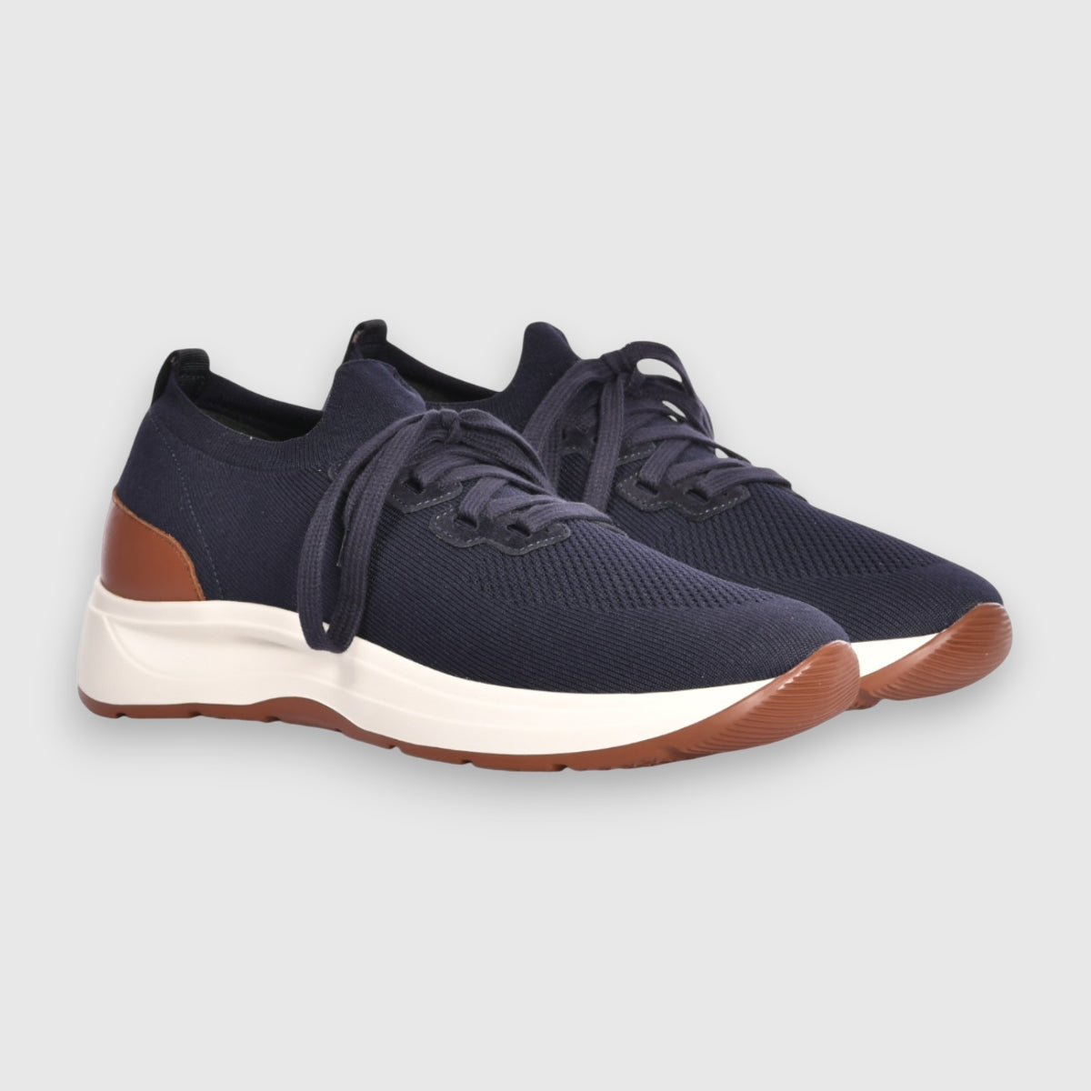Gran Sasso Navy Blue Knitted Sneakers feature breathable knit fabric, white soles, brown accents on the heel and sole edge, and navy blue laces. Displayed against a plain light gray background. , available at Richard Gelding Mayfair