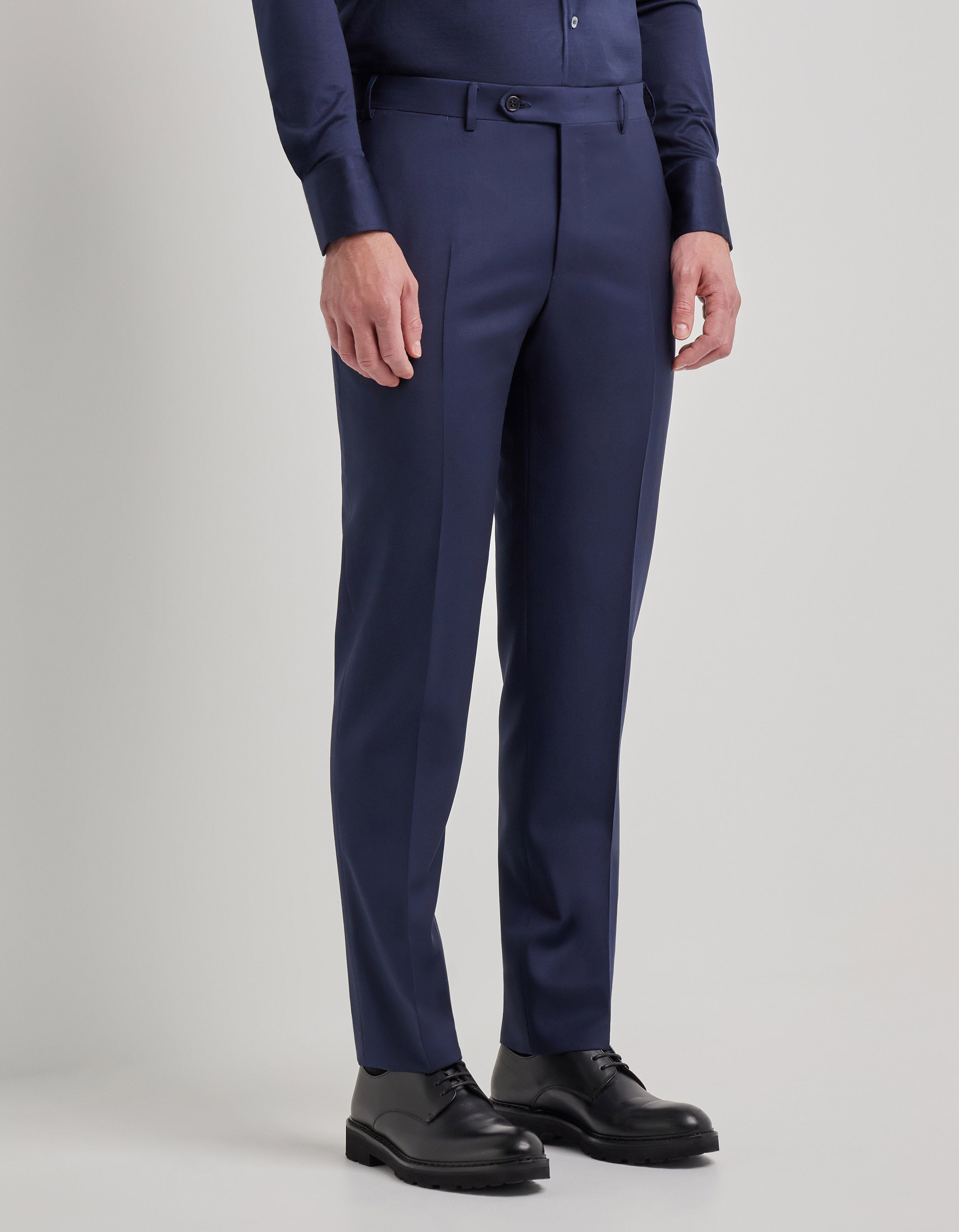 A man wears a Canali Blue Wool Twill Single Breasted Suit against a plain background. Only his body from chest to feet is visible, with his hands relaxed at his sides and black leather dress shoes completing the look. , available at Richard Gelding Mayfair