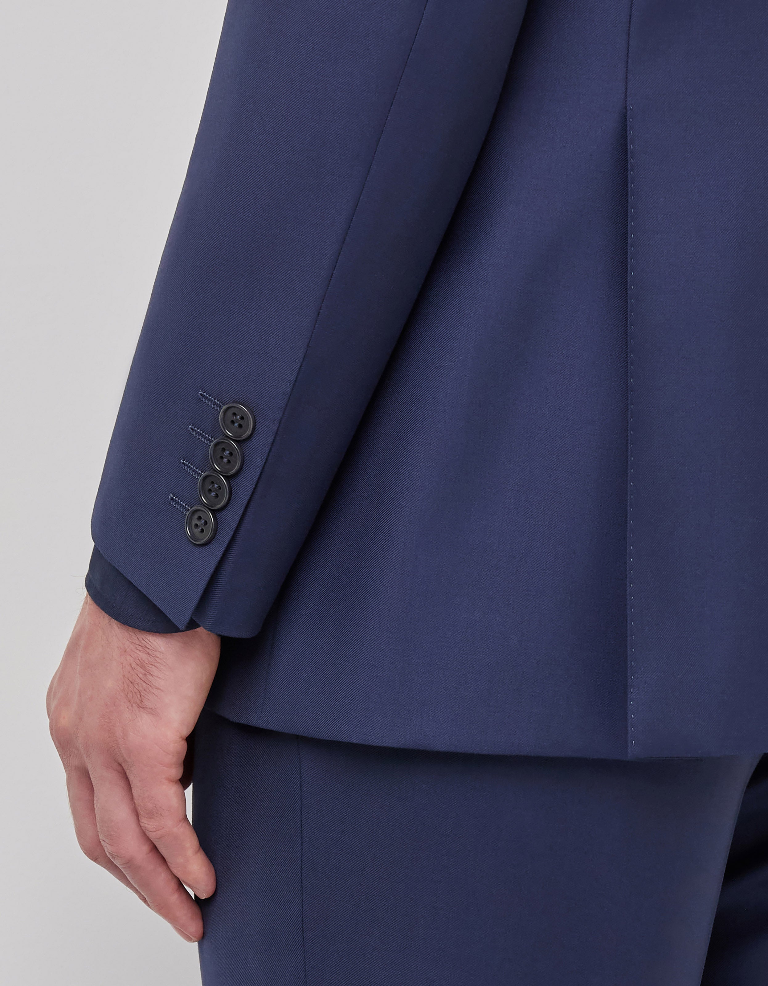 A close-up shows a person’s left arm and hand in a Canali Blue Wool Twill Single Breasted Suit. The dark blue jacket has four black sleeve buttons, with crisp tailoring and smooth fabric, set against a plain light background. , available at Richard Gelding Mayfair