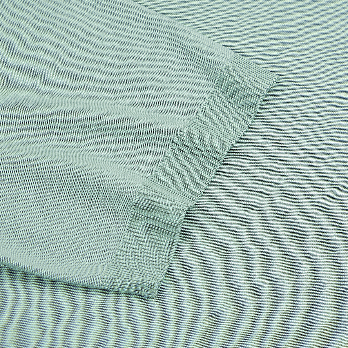 Close-up of Altea’s Green Lyocell T-shirt, featuring the ribbed cuff of a long sleeve on a flat surface. The soft, mint-green knit and fine ribbing highlight the T-shirt’s stretch and smooth texture. , available at Richard Gelding Mayfair