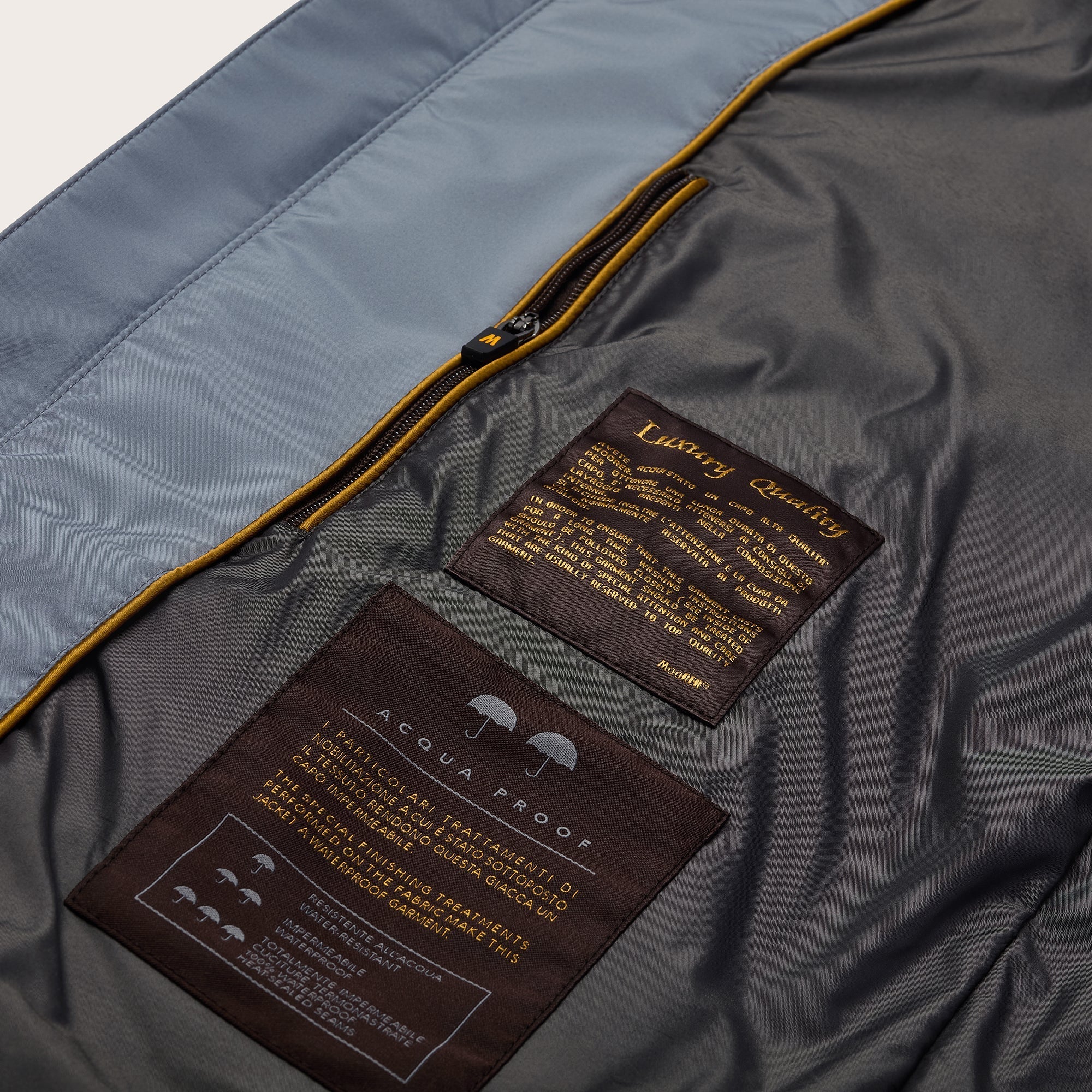 Close-up of the Navy Blueberry Nylon Alcide Blouson's inner lining, featuring two brown Moorer fabric labels with gold text and a yellow-trimmed zip pocket. The larger label reads Acqua Proof; the smaller says Luxury Quality with care instructions. , available at Richard Gelding Mayfair