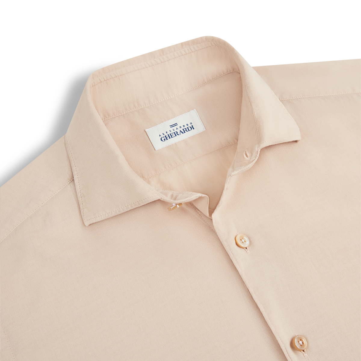 A neatly folded Beige Muslin Beach Shirt with a pointed collar and light buttons is displayed on a white background. The inside collar label shows Alessandro Gherardi in blue text. , available at Richard Gelding Mayfair