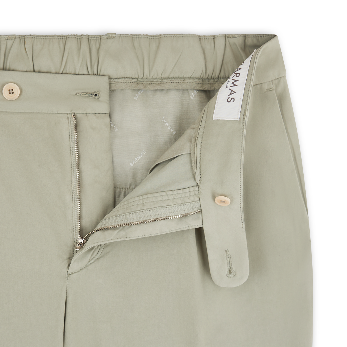 A close-up of sage green cotton/silk chinos by Barmas, featuring an open zipper fly, beige button closure, and a stretch waistband at the back. A fabric label with "Barmas" is sewn inside, with subtle branding text on the inner lining. , available at Richard Gelding Mayfair