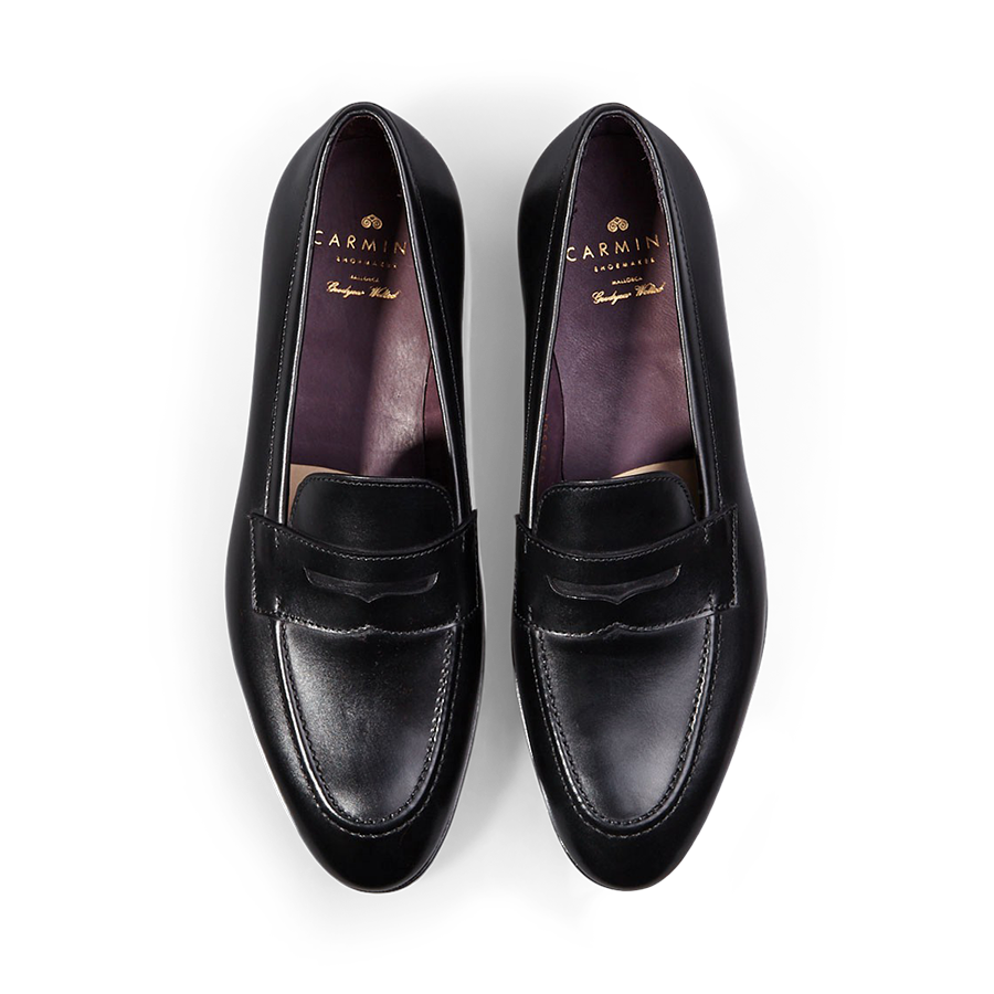 A pair of Carmina black calf leather Uetam penny loafers against a black background.