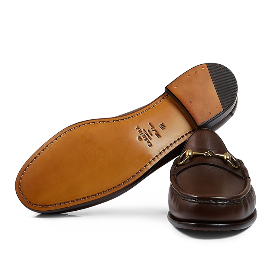 A pair of brown Carmina leather Xim horsebit loafers with gold-tone hardware, placed against a transparent background.