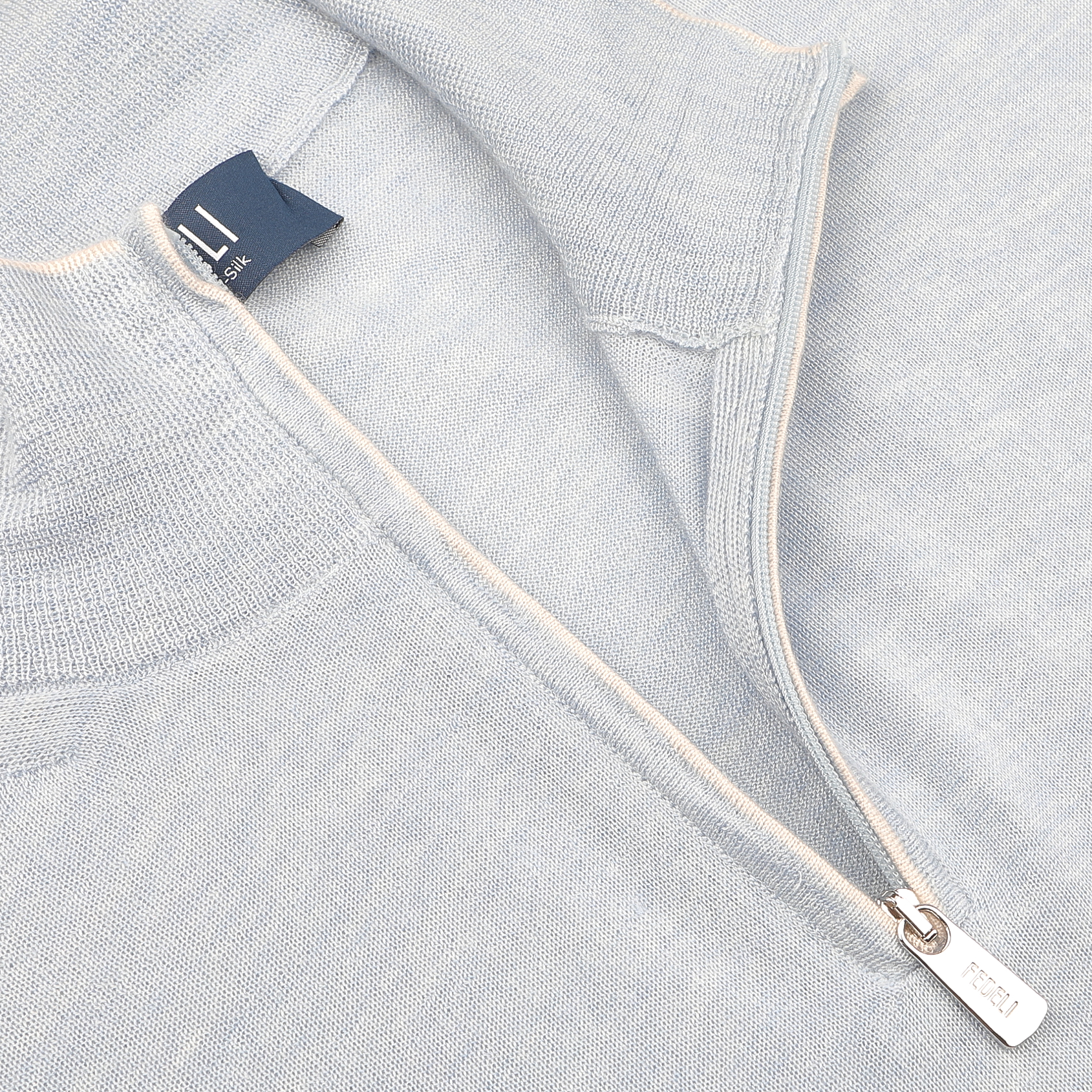 Close-up of Fedeli's Sky Blue Cashmere Silk 1/4 Zip Sweater, showcasing a small metal pull tab and a visible clothing tag.