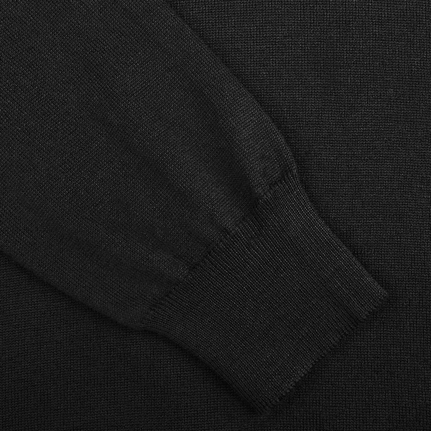 Close-up of the Gran Sasso Black Extra Fine Merino Wool Rollneck, featuring a ribbed sleeve cuff and slim fit design against a matching black background.