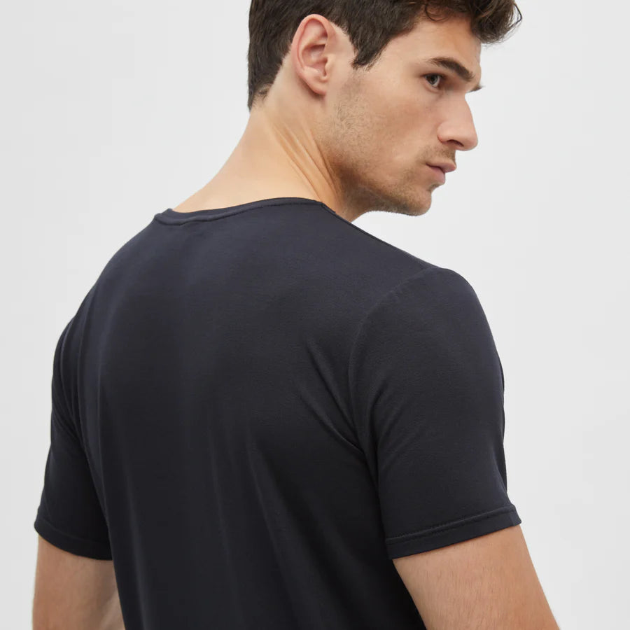 A young man with short brown hair, shown from the back and turning right, wears a fitted Homebody Black Modal Classic Short Sleeve T-Shirt. The plain white background keeps attention on him and his base layer. , available at Richard Gelding Mayfair