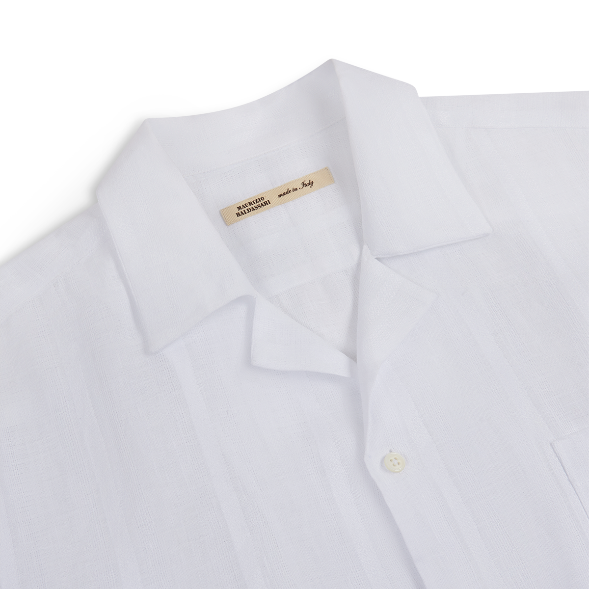 A close-up of the Maurizio Baldassari White Linen Short Sleeve Bowling Shirt, featuring a chest pocket, visible white button, and a “Made in Italy” tag inside the collar; set against a plain white background. , available at Richard Gelding Mayfair