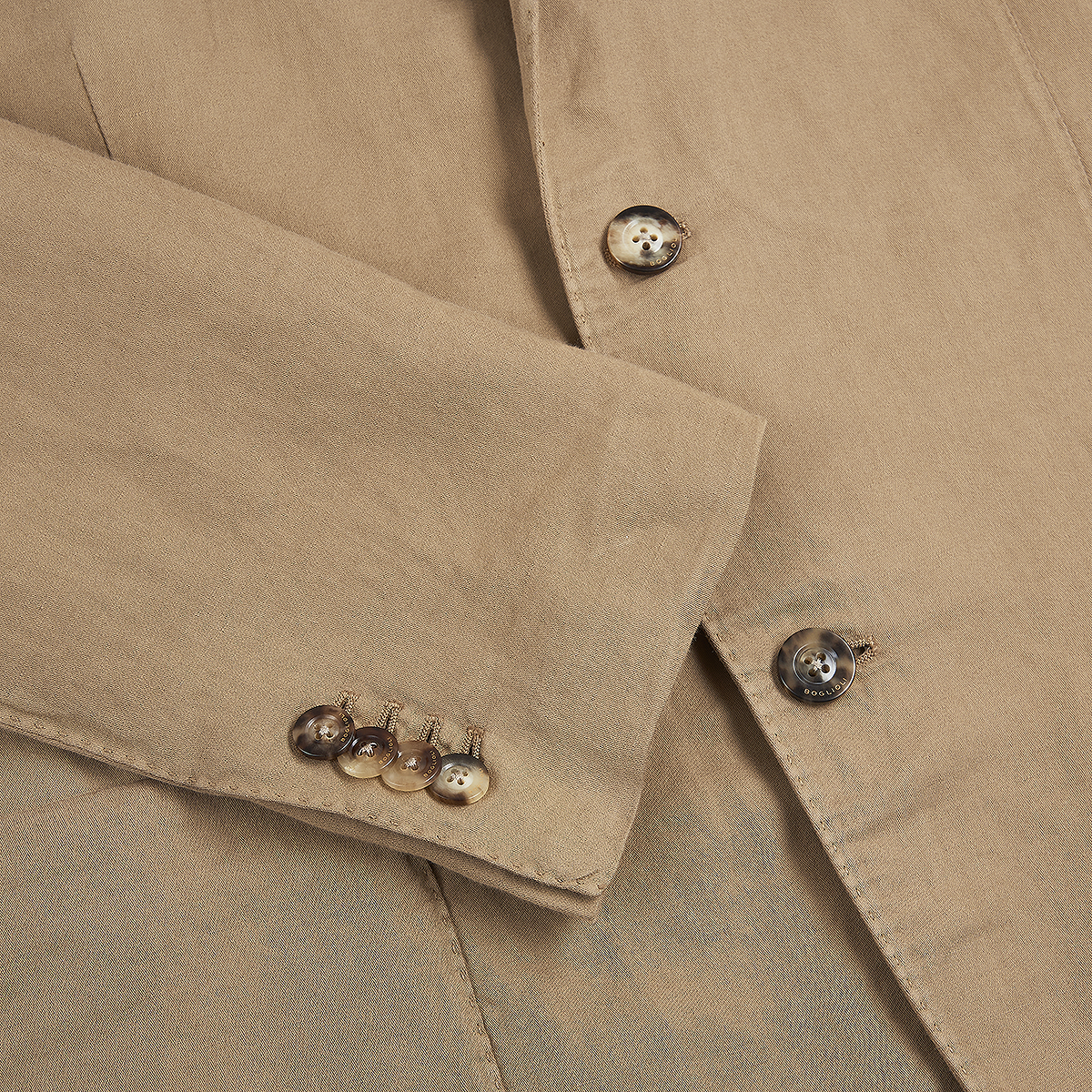 Close-up of the Boglioli Camel Beige Satin Cotton/Linen Jacket, featuring textured fabric. The sleeve shows four shiny metal buttons; the front displays two matching buttons and a seam, emphasizing its tailored construction. , available at Richard Gelding Mayfair