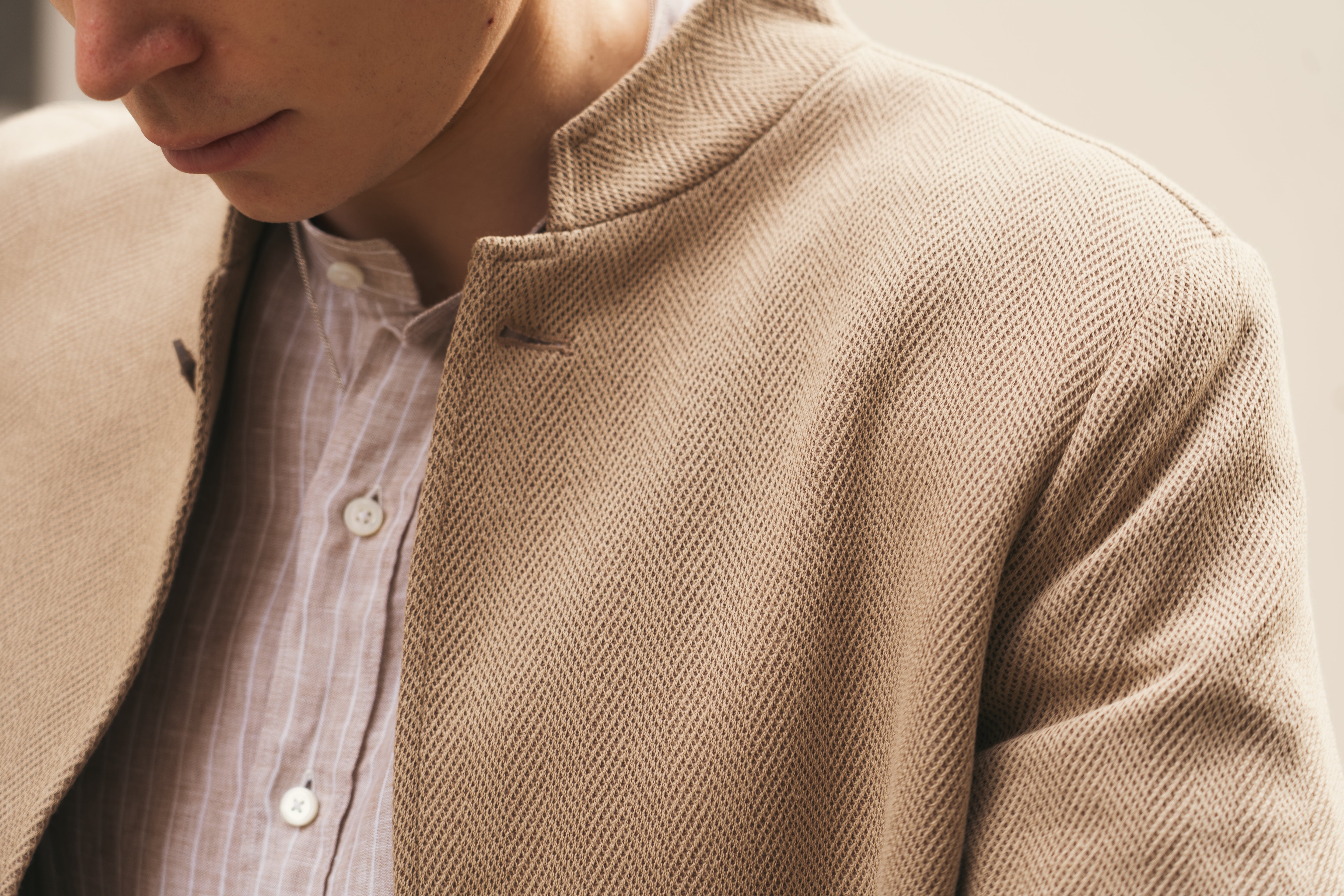 Close-up of a person in a Gran Sasso Beige Herringbone Cotton Blend Jacket over a light-striped shirt with white buttons. The partial view highlights the refined fabric and classic style of this timeless piece. , available at Richard Gelding Mayfair