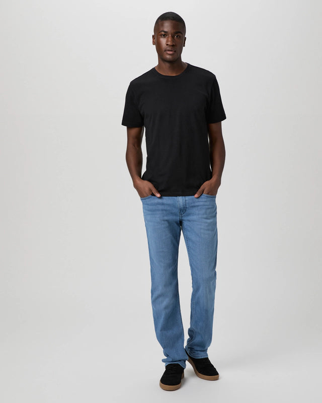A man stands facing forward against a plain light gray background, wearing the Paige Black Cotton Sorden Crew Neck T-Shirt with light blue jeans and black shoes. His hands are in his pockets and he has a neutral expression. , available at Richard Gelding Mayfair