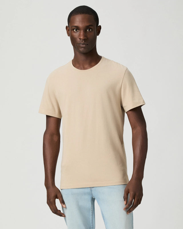 A person stands facing forward against a white background, wearing the Paige Natural Beige Cotton Sorden Crew Neck T-Shirt and light blue jeans. Their arms are relaxed at their sides, with a neutral expression and no accessories in a well-lit scene. , available at Richard Gelding Mayfair