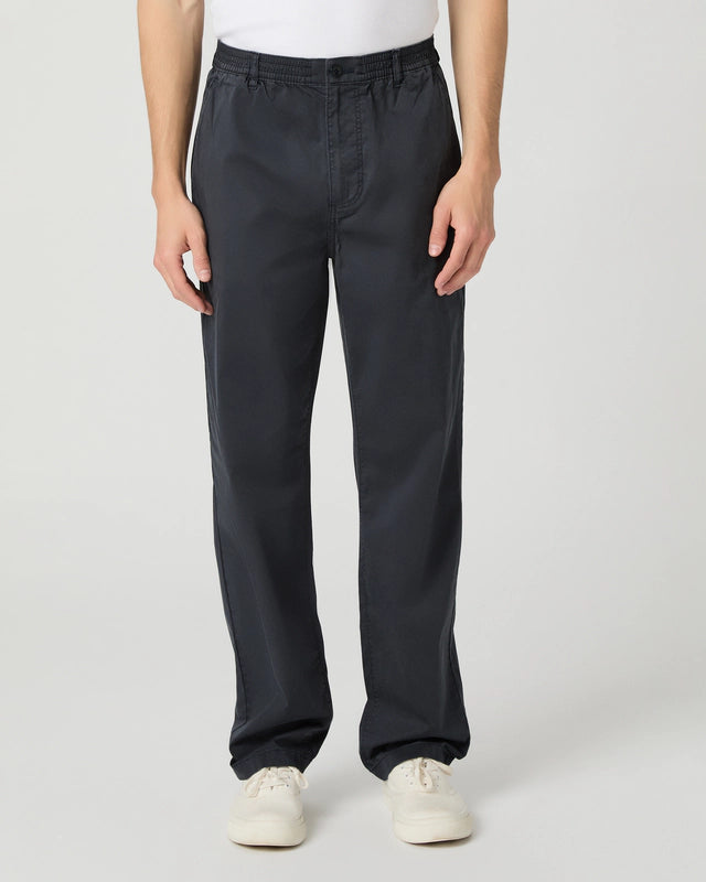 A person stands facing forward, wearing Paige Navy Cotton Stretch 'Eberton' Trousers with a straight-leg cut and elastic waistband. Paired with white casual shoes, the upper body is mostly out of frame against a plain, light background. , available at Richard Gelding Mayfair
