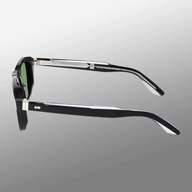 A side view of Ply Black | Green sunglasses by TBD Eyewear is shown against a smooth gray background. The black frames feature green lenses and handcrafted temples with engraved silver metal sections and logo detailing. , available at Richard Gelding Mayfair
