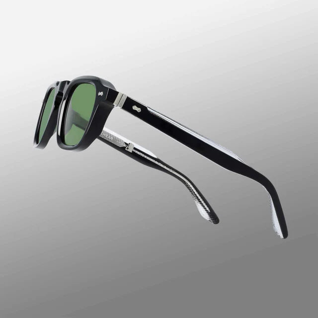 The Ply Black | Green by TBD Eyewear are handcrafted Italian sunglasses featuring green-tinted rectangular lenses, glossy black thick frames, silver hinges, and a metallic accent near the arms, shown on a gradient gray background. , available at Richard Gelding Mayfair