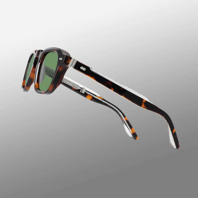 Ply Brown Havana | Green sunglasses by TBD Eyewear are angled sideways against a gray gradient background. They feature a thick, handcrafted acetate renew frame in brown havana with green lenses and partially open temples showing silver hinges. , available at Richard Gelding Mayfair