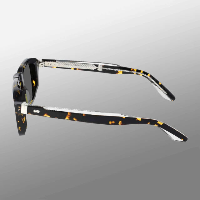 The TBD Eyewear Ply Black Havana | Grey sunglasses are handcrafted in Italy with dark lenses and black-yellow tortoiseshell Acetate Renew arms, metallic hinges, and textured silver accents, shown folded on a gray gradient background. , available at Richard Gelding Mayfair
