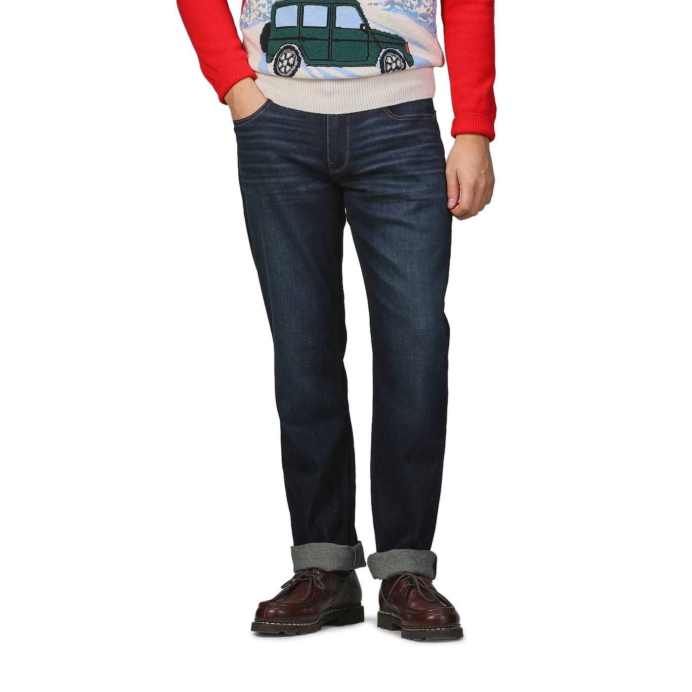 A person dressed in the Paige Blue Faded Cotton Cramer Normandie Jeans, accompanied by a red sweater featuring a car design, and brown shoes stands against a gray background.