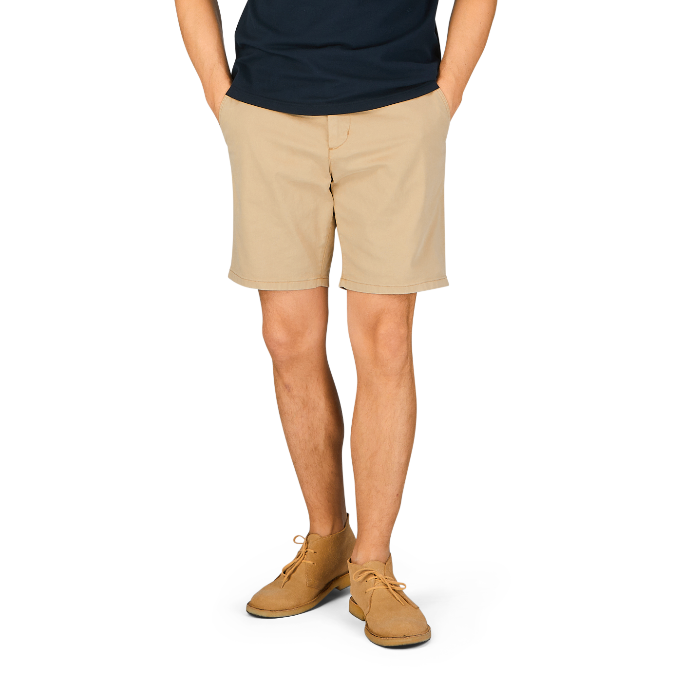 A person standing with their hands behind their back, wearing a navy blue t-shirt, Paige Khaki Beige Cotton Blend Phillips shorts, and light brown shoes.