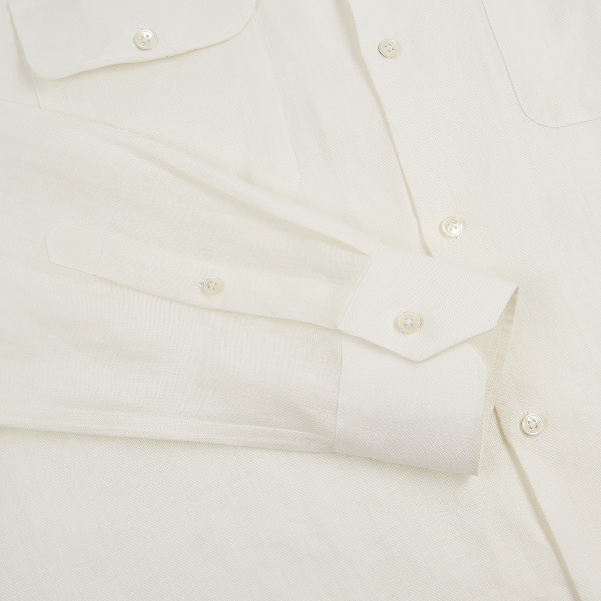 A close-up of the Maurizio Baldassari White Linen Army Shirt laid flat, showing its textured weave, buttoned cuff, pearly buttons, and two chest pockets. , available at Richard Gelding Mayfair