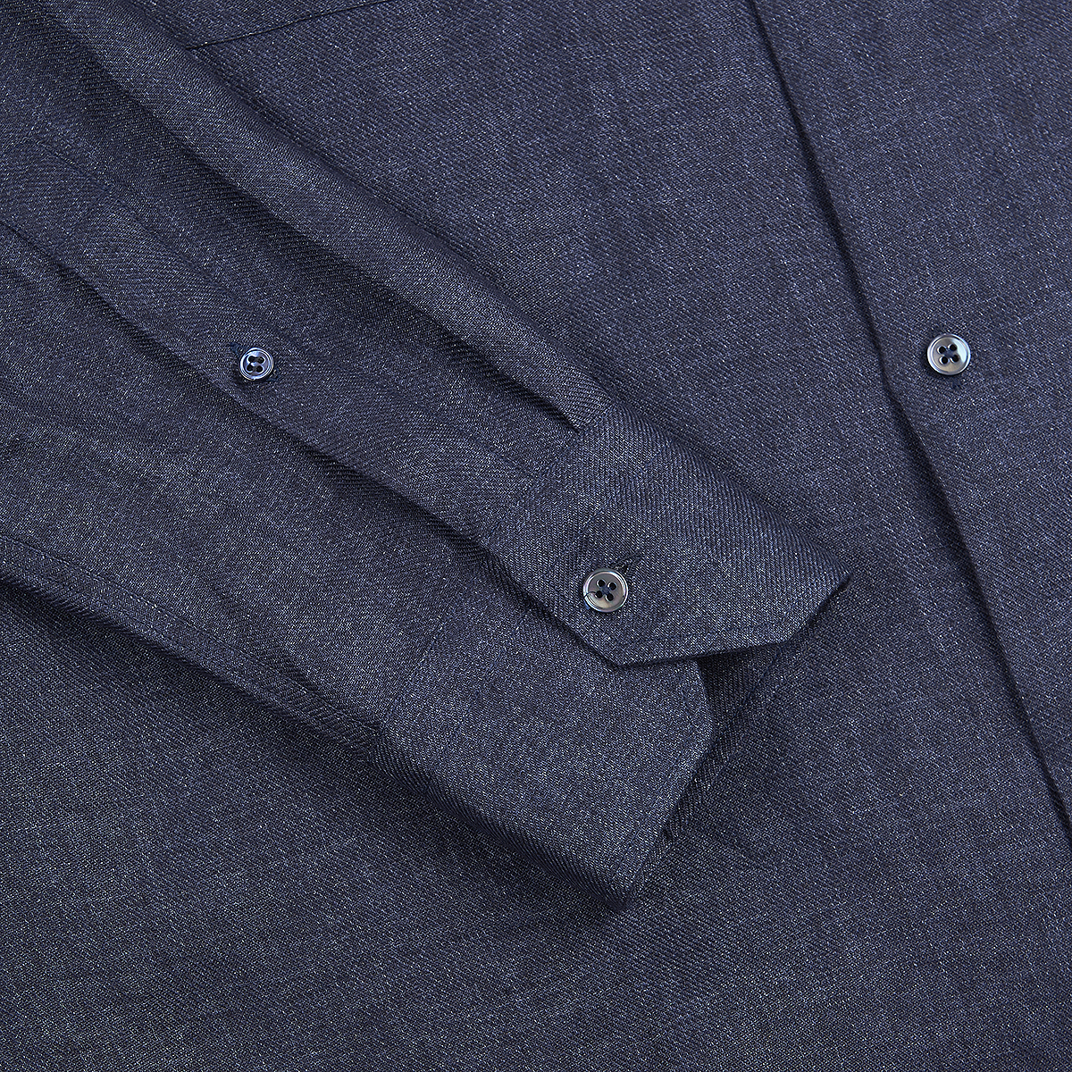 A close-up of the Maurizio Baldassari Denim Blue Linen Army Shirt highlights its textured, heathered fabric, crisp finish, and black buttons on a folded sleeve. The shirt appears neatly pressed and stylishly detailed. , available at Richard Gelding Mayfair