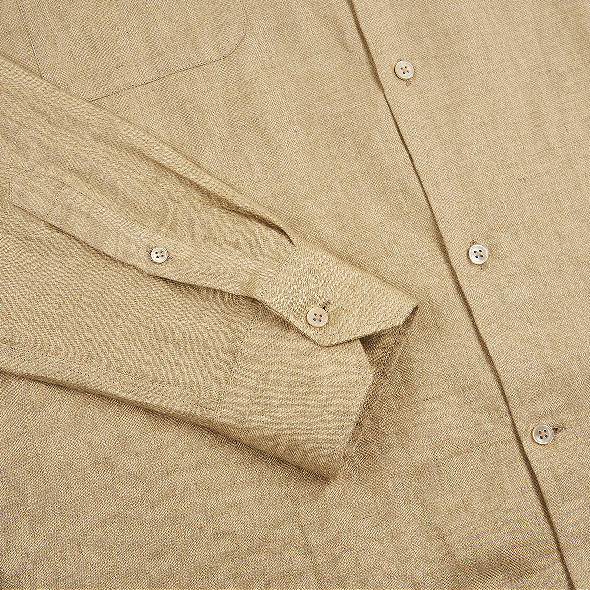 A close-up of the Maurizio Baldassari Beige Linen Army Shirt highlights the textured fabric, light buttons, chest pocket, clean stitching, and a long sleeve with a buttoned cuff laid flat. , available at Richard Gelding Mayfair