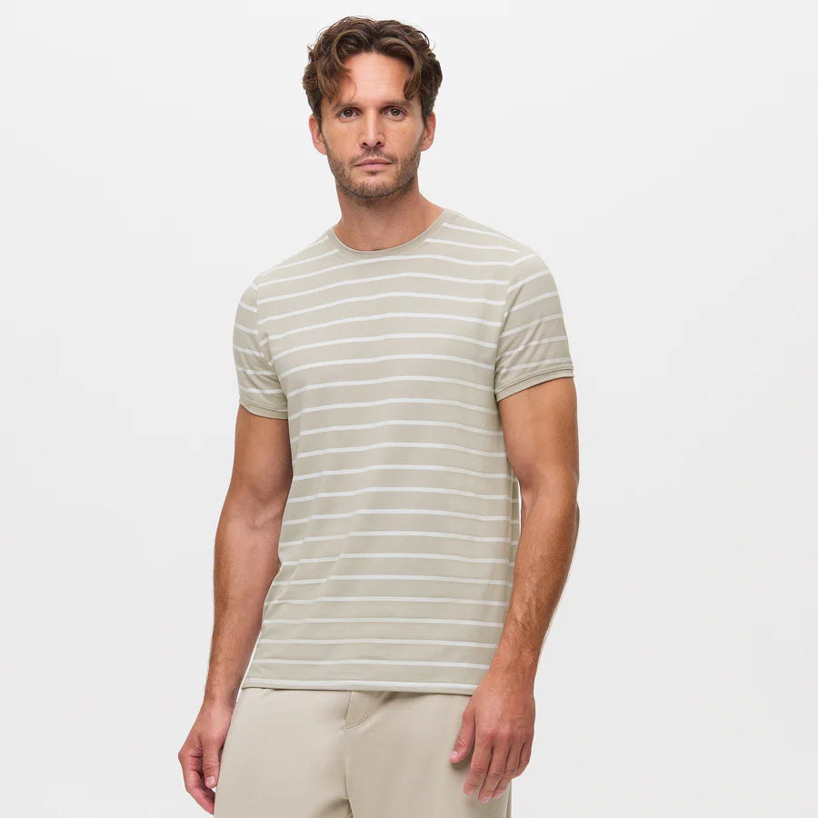 A man with light skin and wavy brown hair wears the Homebody Beige Desert Stripe Modal Marlow Striped T-Shirt. He stands facing forward against a plain white background with a neutral expression, one hand by his side. , available at Richard Gelding Mayfair