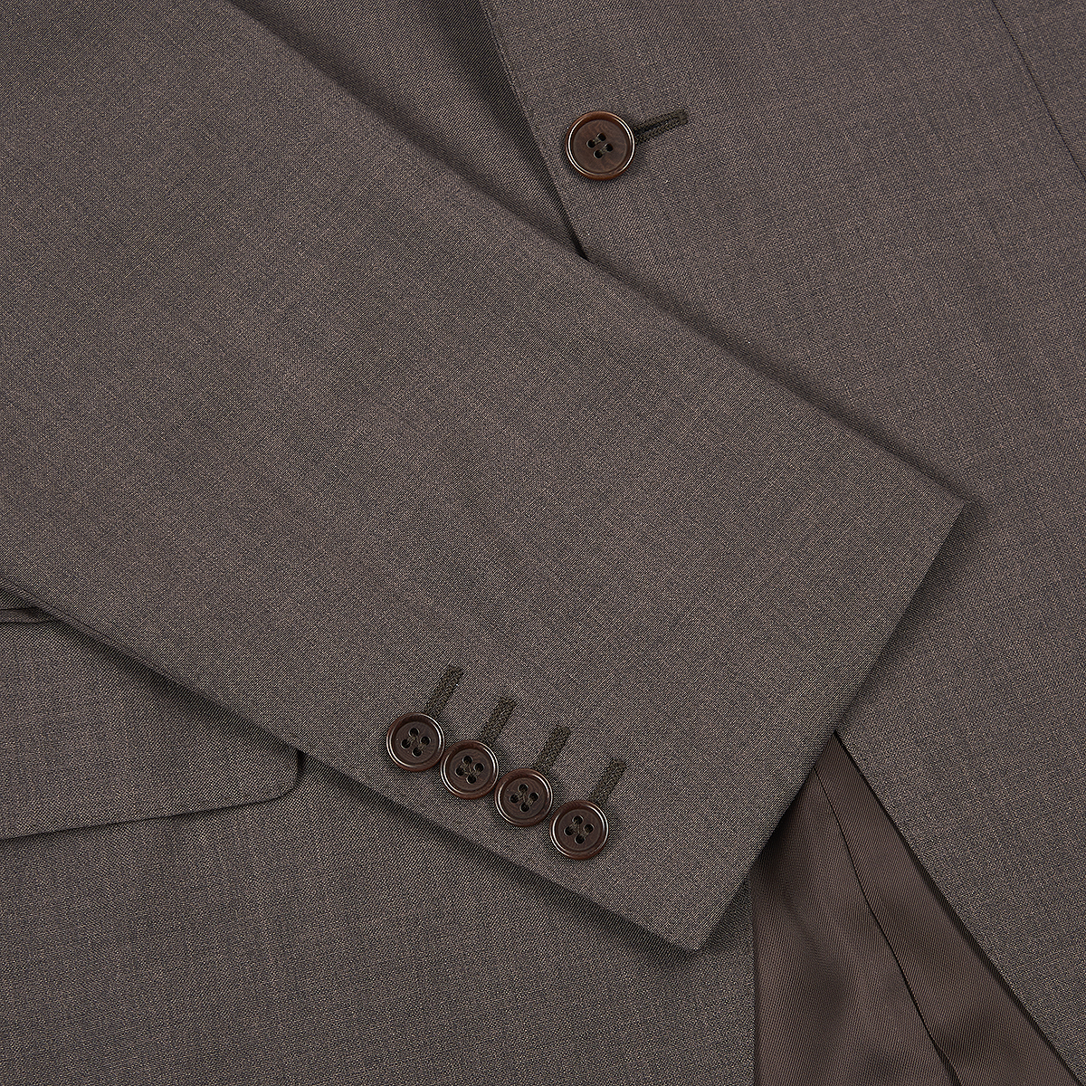 Close-up of the Canali Dark Brown Tropical Wool Suit shows a men’s brown jacket sleeve with four matching cuff buttons, textured wool fabric, two front buttons, a pocket flap, and visible brown satin lining. , available at Richard Gelding Mayfair