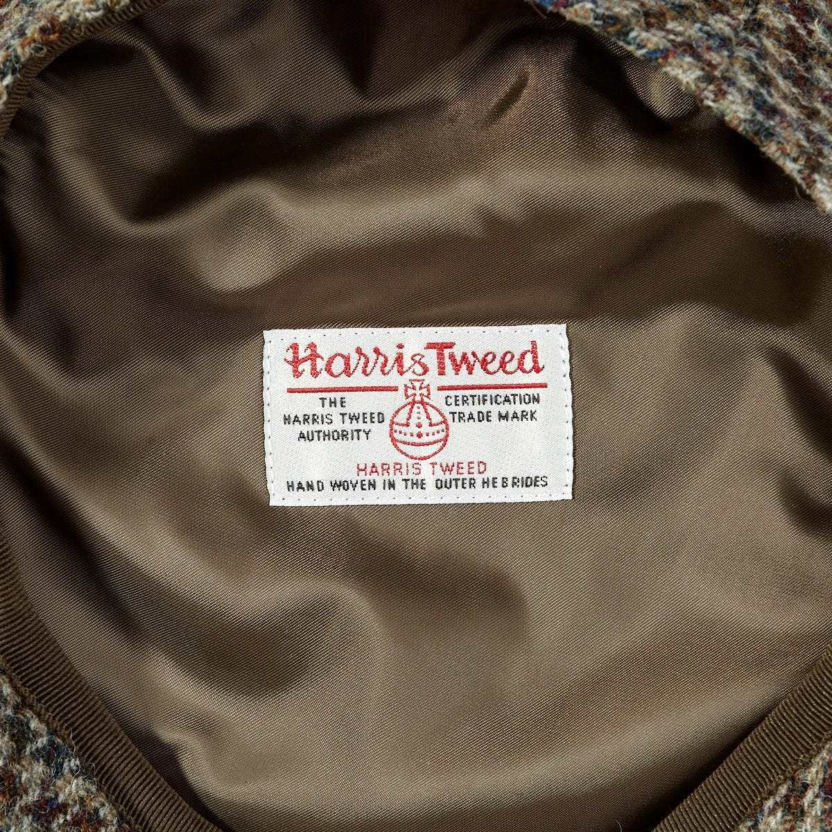 A brown tweed jacket with a Beige Houndstooth Harris Tweed Ivy Contemporary Cap by Wigéns label on it.