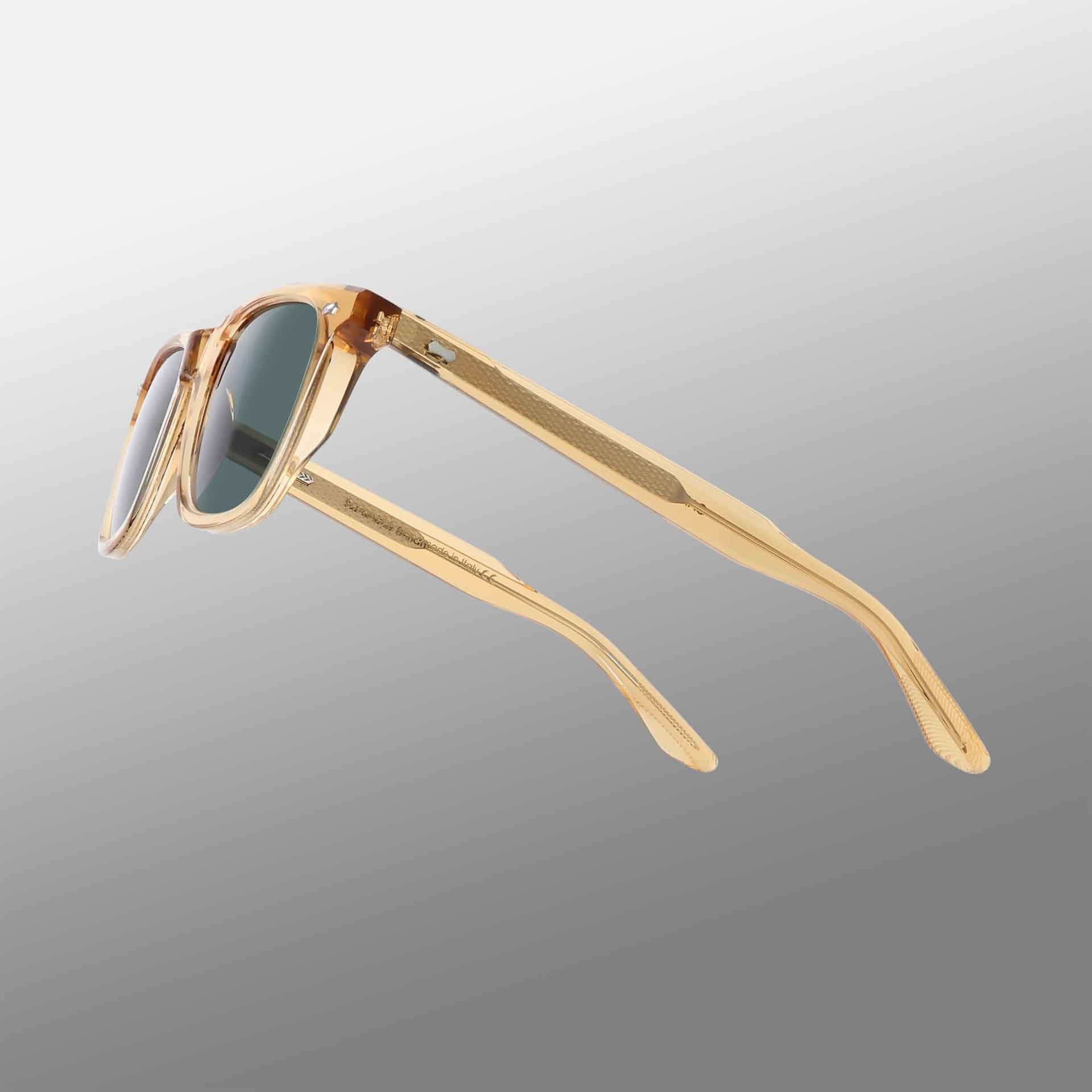 The Carré Eco Champagne | Bottle Green sunglasses by TBD Eyewear feature transparent amber frames and dark rectangular lenses, displayed angled on a gray gradient. Their slightly curved arms have a ribbed texture on the inner side. , available at Richard Gelding Mayfair