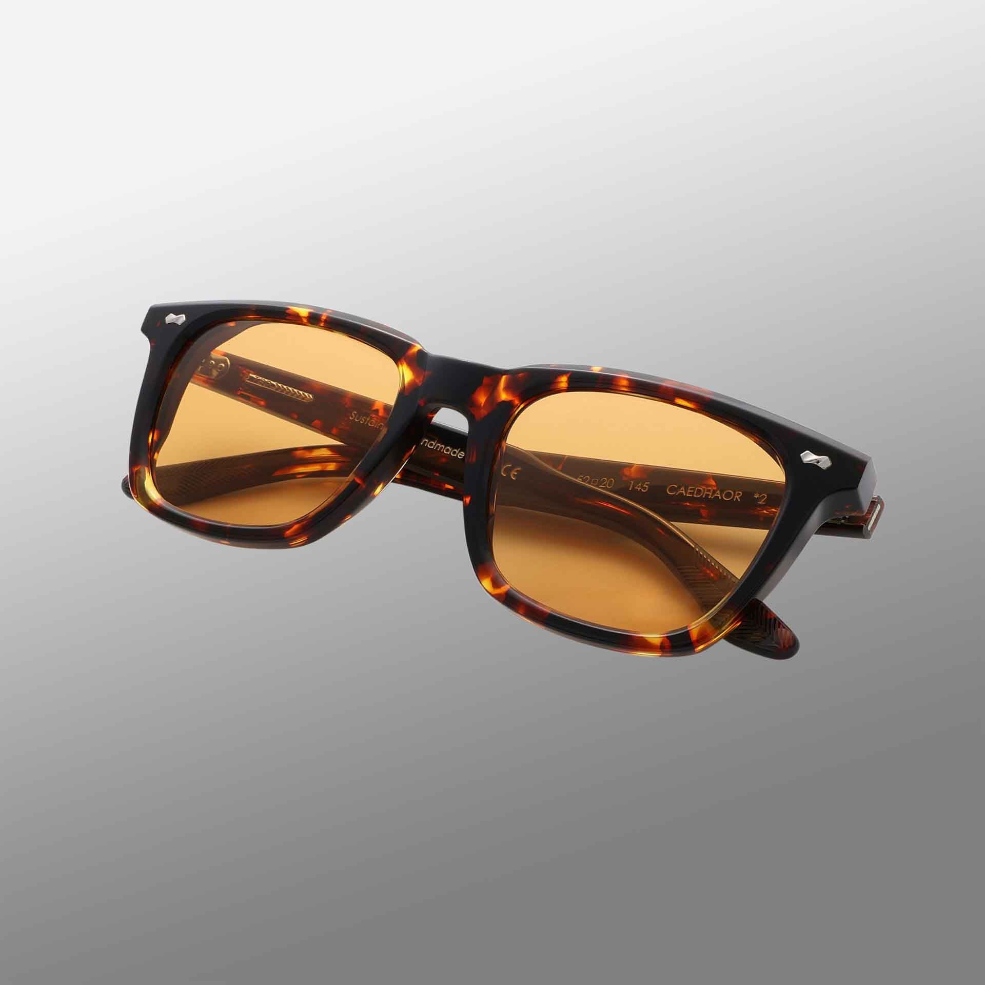 The Carré Eco Dark Havana | Orange sunglasses by TBD Eyewear feature a thick, tortoiseshell-patterned frame and rectangular amber-tinted lenses, showcased at an angle against a smooth gray gradient background. , available at Richard Gelding Mayfair