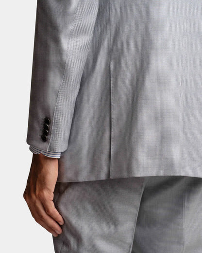 A close-up of a person wearing the Cavour Pale Blue Wool/Silk Puppytooth Suit from behind shows the left arm and side, with three dark buttons at the cuff. The suit's fine texture hints at its premium fabric, and their hand rests relaxed at their side. , available at Richard Gelding Mayfair