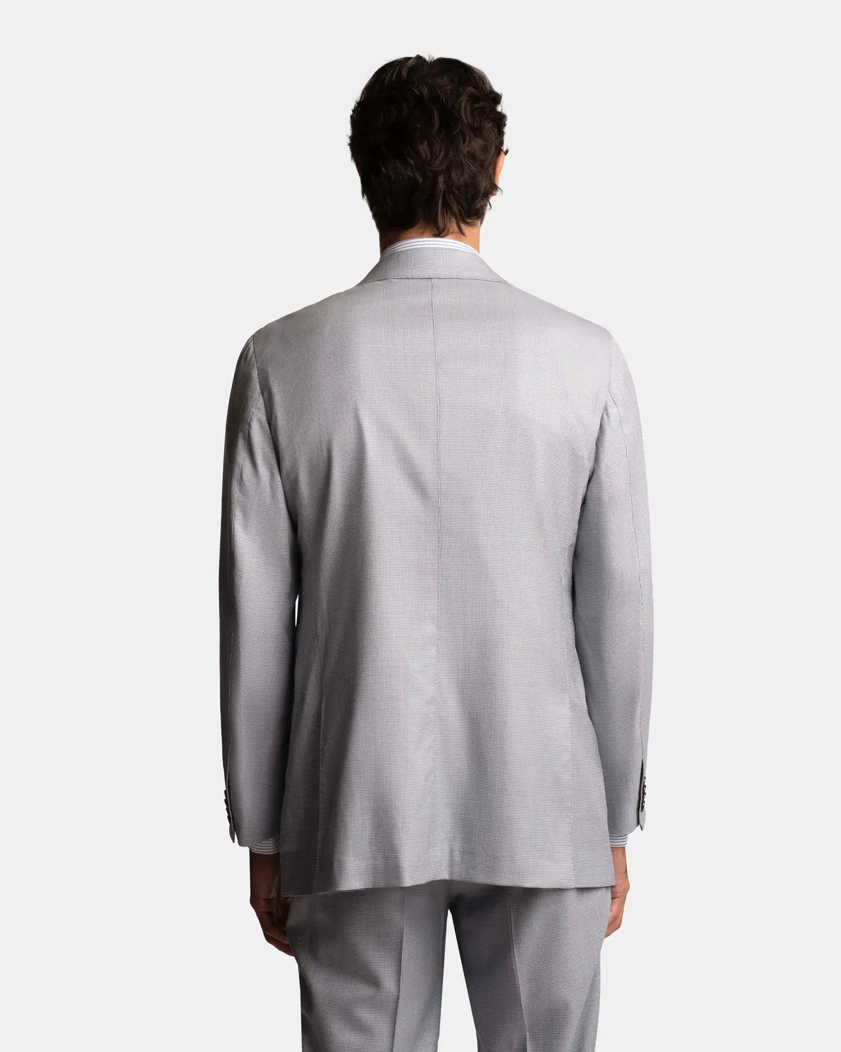 A person with short dark hair faces away, showcasing the relaxed fit of the Cavour Pale Blue Wool/Silk Puppytooth Suit against a plain white background, highlighting the back view of this refined two-piece. , available at Richard Gelding Mayfair