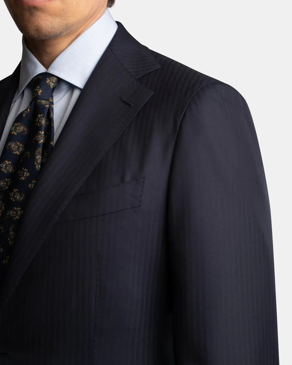 A man is shown from the chest up against a light background, wearing the Cavour Navy Herringbone Super 150's Wool Suit. Only the lower half of his face is visible. , available at Richard Gelding Mayfair