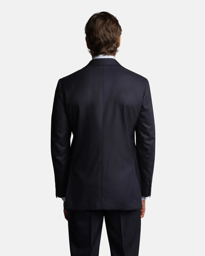 A man faces away on a plain white background, showcasing the Cavour Navy Herringbone Super 150's Wool Suit with matching trousers and a white dress shirt. His brown hair is neatly styled, highlighting the tailored fit from the back. , available at Richard Gelding Mayfair