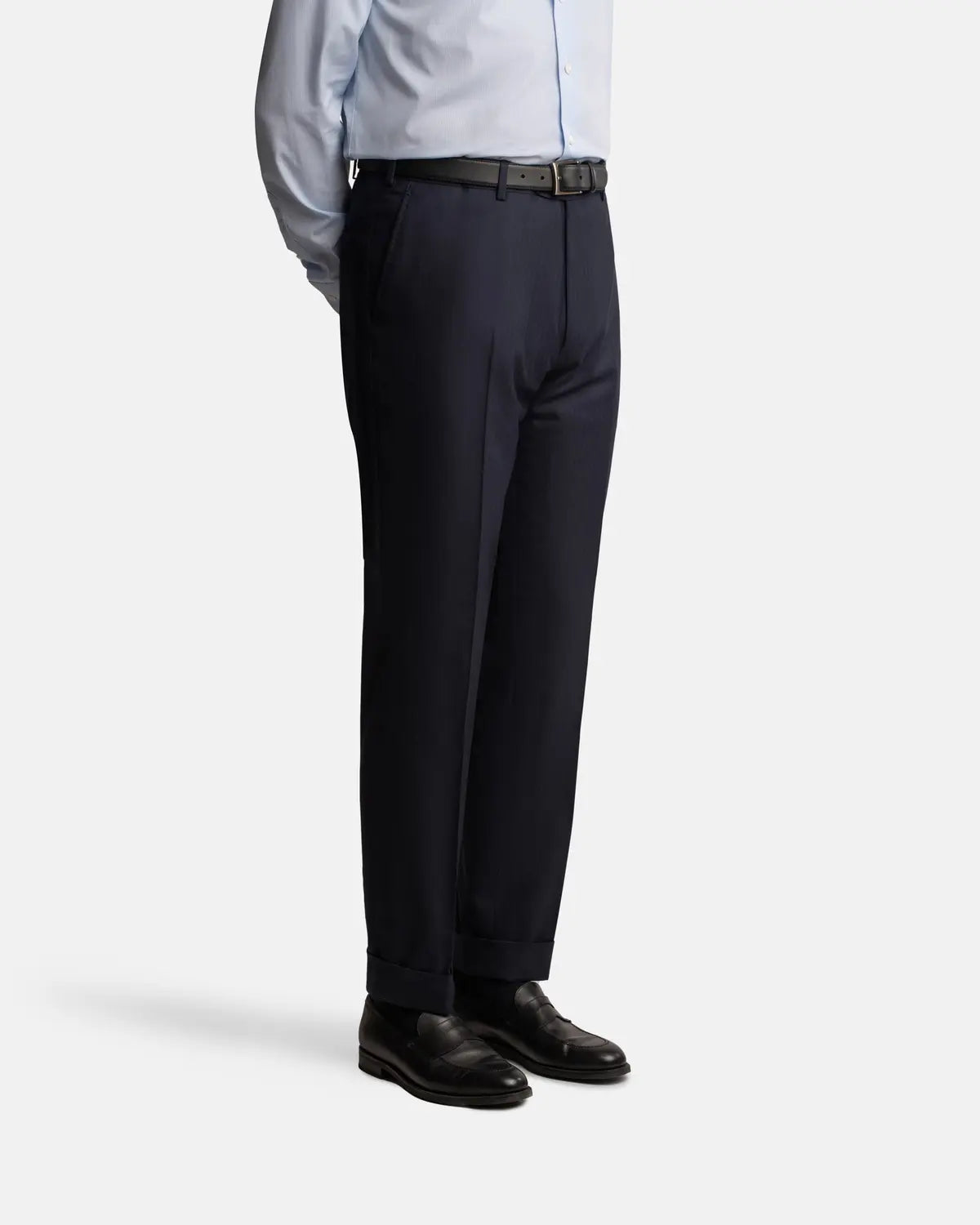 A person stands with arms behind their back, wearing Cavour's Navy Herringbone Super 150's Wool Suit. The image, cropped just below the shoulders, features a plain light background. , available at Richard Gelding Mayfair