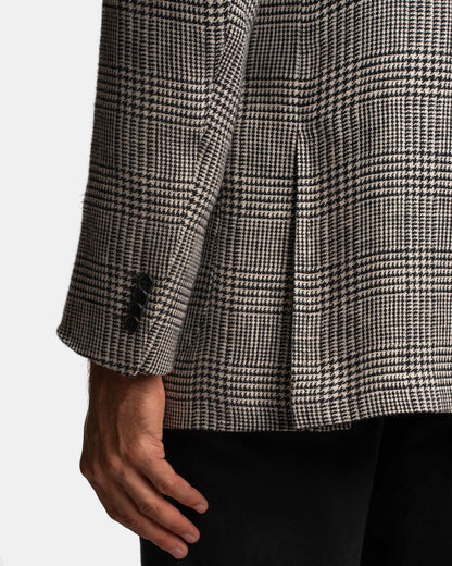 A close-up of a person’s arm wearing the Cavour Black/Grey Linen Glencheck Blazer with three black sleeve buttons, paired with black pants against a plain white background. Their hand rests relaxed at their side. , available at Richard Gelding Mayfair
