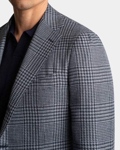A close-up shows a man in a Cavour Blue Glencheck Wool/Silk/Linen Blazer over a dark navy collared shirt, with only his lower face and upper torso visible against a plain light background. , available at Richard Gelding Mayfair