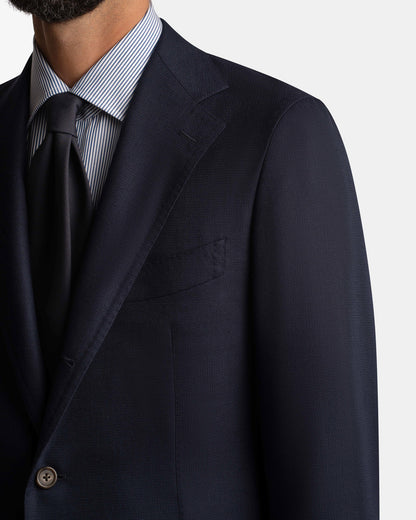 A close-up shows a man in a Cavour Navy Hopsack Wool Blazer over a blue and white striped shirt with a dark tie, focusing on the blazer’s tailored upper chest and shoulder, with his face partially visible. , available at Richard Gelding Mayfair
