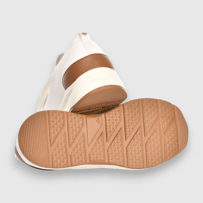 A close-up showcases the Gran Sasso White Knitted Sneaker, highlighting its textured tan rubber sole with zigzag and diamond patterns, brown heel accent, and white knit upper against a light gray background. , available at Richard Gelding Mayfair
