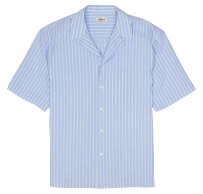 The Altea Baby Blue Cotton Seersucker Cuban Shirt features white vertical stripes, a relaxed collar, left chest pocket, and five white buttons. The shirt is neatly laid flat on a white background. , available at Richard Gelding Mayfair