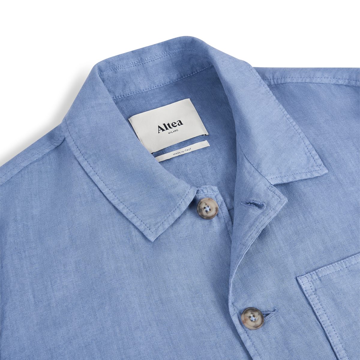 Close-up of the Sugar Packet Blue Linen Chore Jacket by Altea, featuring a pointed collar, brown buttons, chest pocket, and a white Altea label inside the collar. The refined Italian style stands out against a white background. , available at Richard Gelding Mayfair
