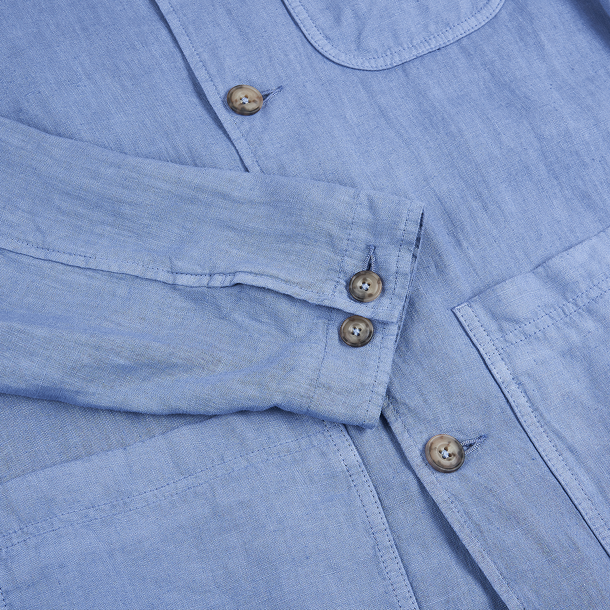 Close-up of the Altea Sugar Packet Blue Linen Chore Jacket, featuring a long sleeve with two brown cuff buttons, buttonholes, and a chest pocket. The soft, textured linen recalls relaxed Italian style. , available at Richard Gelding Mayfair