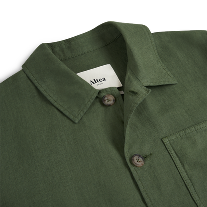 A close-up of the Altea Army Green Linen Chore Jacket, made from textured fabric with two buttons and a chest pocket, is neatly laid flat on a white background. The inside label displays the Altea brand. , available at Richard Gelding Mayfair