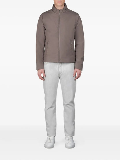 A person stands facing forward in a Moorer Ivory Avorio Nylon Alcide Blouson, light gray jeans, and white sneakers. Their arms are relaxed at their sides against a plain white background, showcasing the casual outfit. , available at Richard Gelding Mayfair