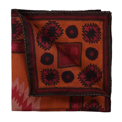 The Amanda Christensen Silk pocket square with Inca inspired pattern boasts an orange background adorned with red and dark brown geometric motifs such as zigzags, diamonds, and circles. Finished with a dark brown stitched border, the handkerchief is presented neatly folded. , available at Richard Gelding Mayfair